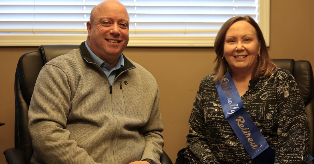 Robert Haynes and Judy Harrison sitting next to one another in an office setting celebrating Judy's retirement.